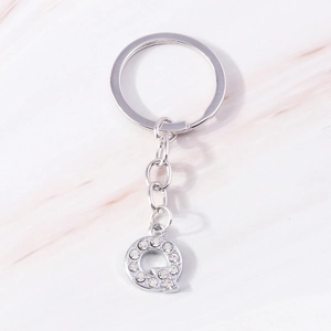 Detail of silver letter Q keychain with sparkling crystal rhinestones on pink marble background