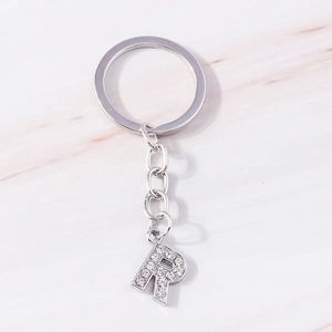 Detail view of crystal rhinestone letter R keychain with silver chain on marble background
