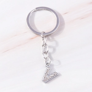 Detailed view of silver letter V keychain with sparkling rhinestones on marble background
