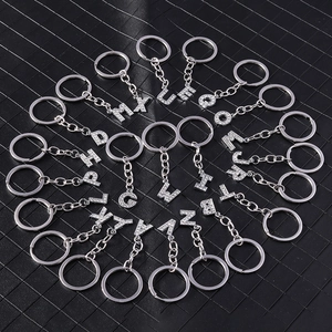 Macro detail of 26 sparkling silver alphabet keychains with white rhinestones on black background