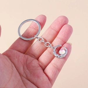 Silver crescent moon keychain with opal stone and star engraving held in hand