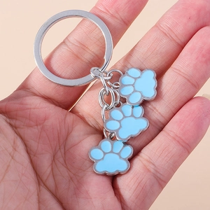 Détail d'un porte-clés tenu à la main avec trois breloques bleues en forme de patte