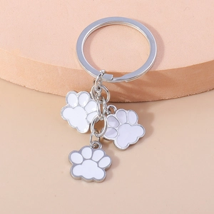 Détail d'un porte-clés argenté avec trois pendentifs pattes en émail blanc sur socle