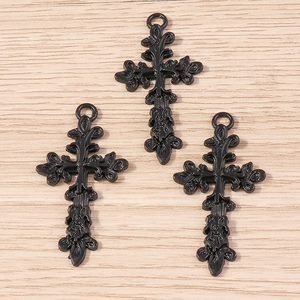 Gros plan de trois pendentifs croix rose ajourée vintage en alliage sur bois clair