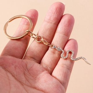 Creative snake keychain in golden metal with sparkling diamonds held in hand