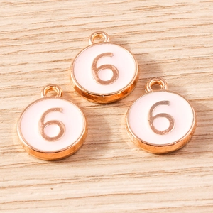 Three rose gold alloy charms with number 6 and white enamel on light wood background