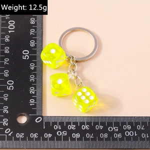 Detail view of yellow acrylic dice keychain weighing 12.5g on a measurement grid