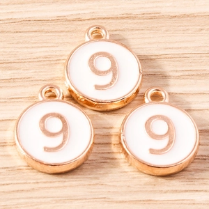 Close-up of circular number 9 charms with gold plating and white enamel on a wooden surface