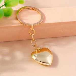 Portachiavi a cuore dorato lucido appoggiato su base rosa con dettaglio di pianta