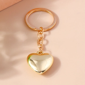 Dettaglio del portachiavi a cuore 3D con placcatura in oro lucido su sfondo di colore tenue