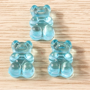 Close-up of three translucent light blue resin gummy bear charms on a wooden surface