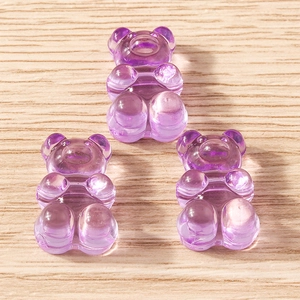 Close-up of three purple translucent resin gummy bear pendants on a light wood background