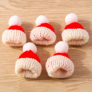 Five mini knitted Christmas hats with white pom-poms on a light wood grain background