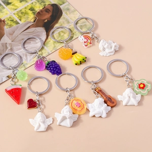 Colorful resin angel and fruit keychain charms displayed on a pink fashion magazine