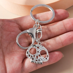 Polished silver skull keychain with lobster clasp and hollow texture on a warm background