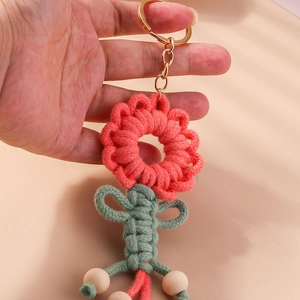 Detail of handmade knitted sunflower keychain with pink petals and wooden beads on a key ring