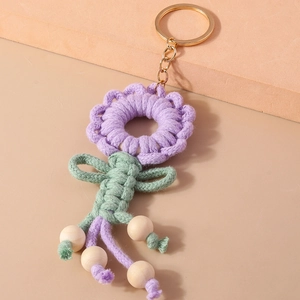 Close-up of handmade purple knitted wreath keychain with green bow and wooden beads