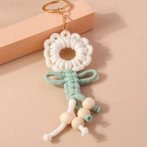 Detail of handmade knit flower keychain with cream petals, sage green bow and wooden beads