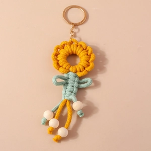 Handmade knitted sunflower keychain with yellow petals and green bow on beige background