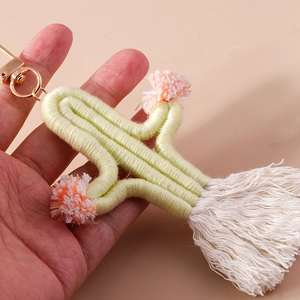 Detail of handmade knit cactus keychain featuring white tassels and soft pink pom poms