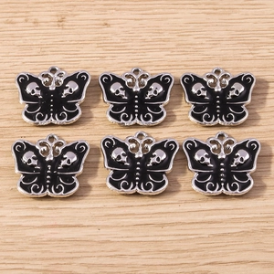 Detailed macro view of 6 gothic black enamel butterfly skull charms on a wooden surface