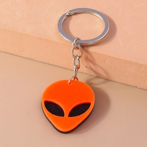 Close-up of orange punk alien keychain with black hollow eyes and silver ring detail