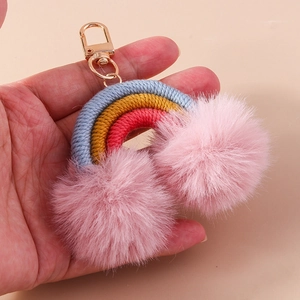 Handheld view of woven rainbow keychain with pink pompoms and gold metal clasp