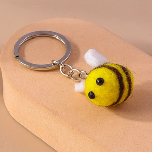 Macro shot of handmade yellow wool felt bee keychain with small wings and silver ring
