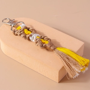 Detail of bohemian handmade cotton tassel keychain with woven yellow and white flower patterns