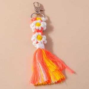 Detail of handmade woven flower keychain with white petals and orange silk tassels