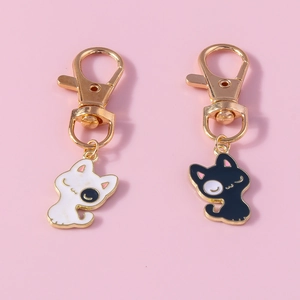 Détail de porte-clés chat noir et blanc mignons avec fermoirs mousquetons dorés sur fond rose