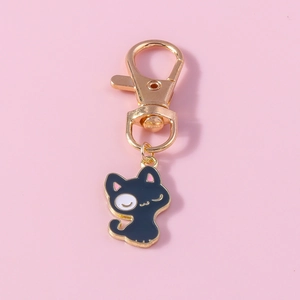Mignon porte-clés chat en émail noir avec fermoir doré sur un fond rose pastel