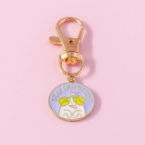 Detail of cute white puppy dog metal keychain with Stay Pawsitive quote on pink base