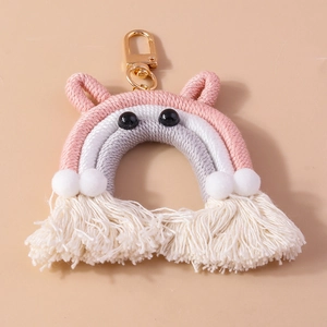 Handmade woven rainbow keychain with pink tassels and white plush pom-poms on a pink background