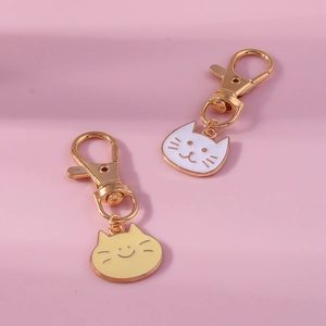 Detail of cute cat charms in white and yellow enamel on golden metal keychains
