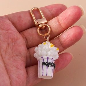 Detail of popcorn keychain featuring a purple striped container and gold lobster clasp
