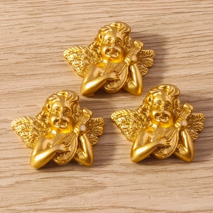 Three gold cupid angel charms with harp and violin details on a light wooden background