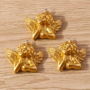 Three matte gold cherub angel pendants with wings and violin on a rustic wooden background