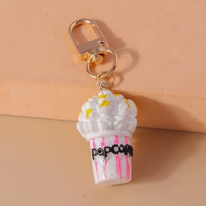 Detail showing a cute popcorn keychain with a golden metal clasp on a dual-tone background