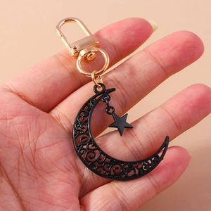 Détail d'un porte-clés lune et étoile noir ajouré avec un fermoir doré tenu à la main