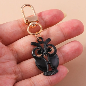 Détail du porte-clés hibou en émail noir avec fermoir doré en forme de D tenu à la main
