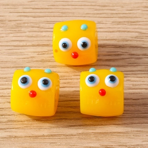 Macro detail of 3 yellow cube cartoon bird charms with blue eyes and antennae for DIY crafts