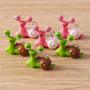 Close-up of pink and green cartoon snail charms with silver hooks on wood background