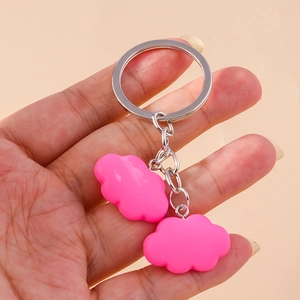 Detailed view of pink resin cloud charms on a silver keychain held by a hand