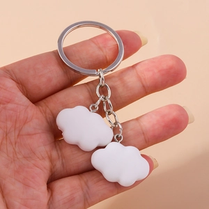 Detail showing two white cloud-shaped resin charms with matte texture on a metal keyring