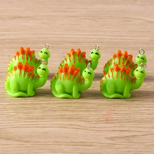 Close-up of six cute green resin dinosaur charms with silver rings on a wood surface