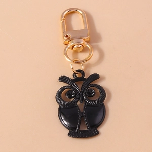 Détail d'un porte-clés hibou noir avec boucle à ressort dorée sur fond rose uni