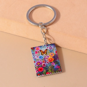Macro detail of square butterfly oil painting keychain with vibrant floral acrylic pendant