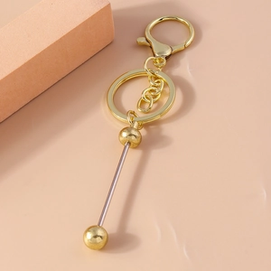 Minimalist gold barbell keychain with lobster clasp on a soft peach-colored surface