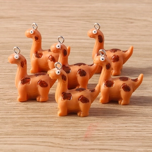 Detailed view of orange resin dinosaur pendants with hanging rings on wood background